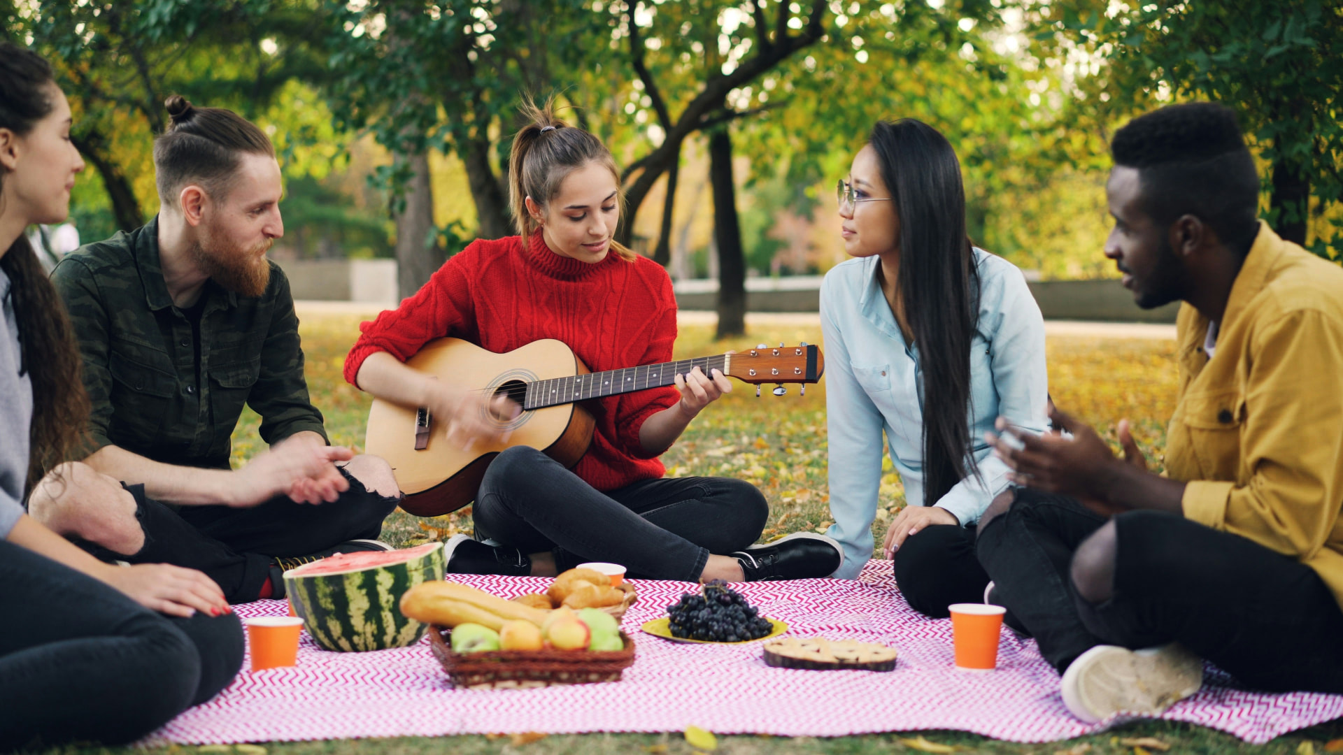 Young people sitting in a circle in a park while one plays guitar